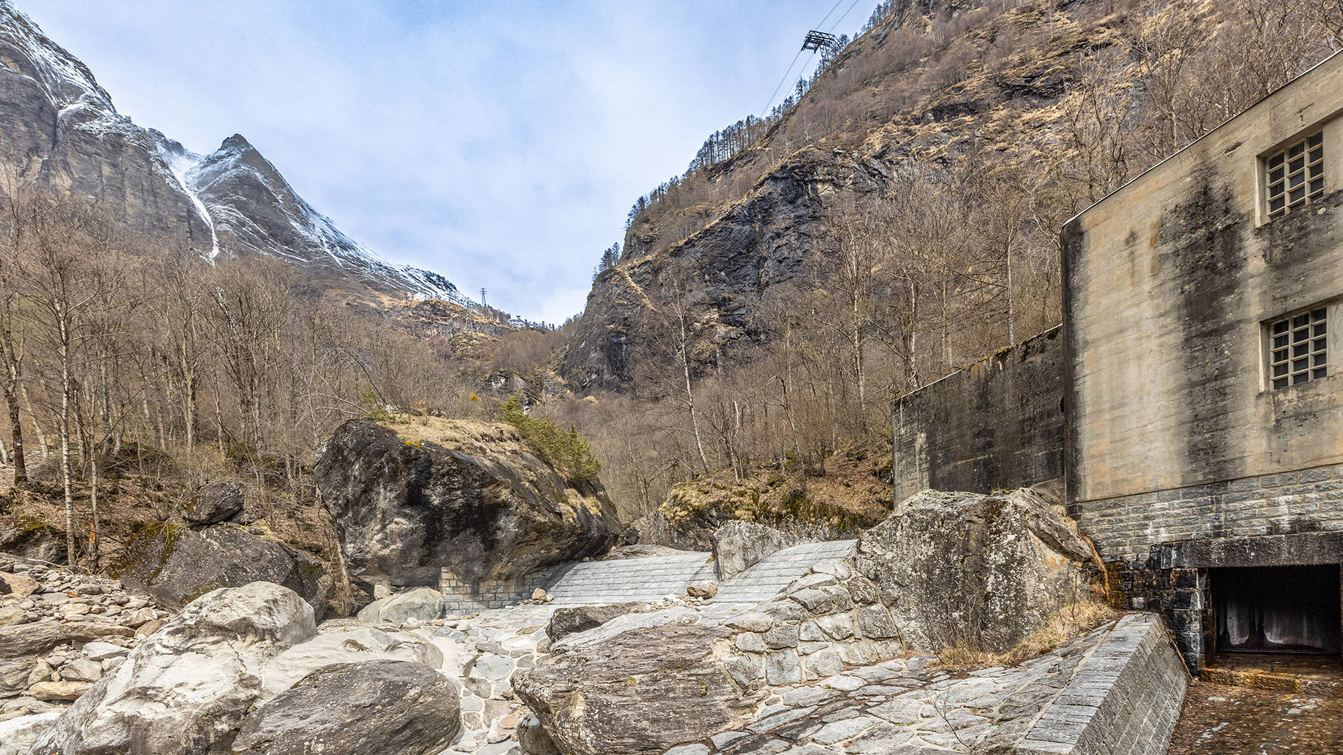 Photograph showing part of a hydropower plant as well as the top of a mountain creek in the Alps with little discharge, a typical situation when water is withheld in the hydropower plant.